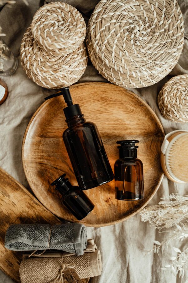 Aesthetic display of brown glass bottles for skincare on a wooden tray with woven baskets.