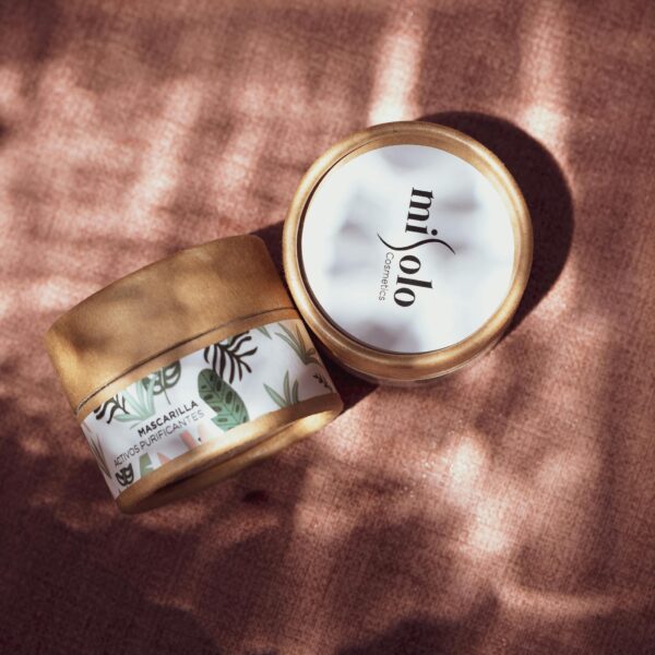 Close-up of cosmetic jars with botanical design under soft sunlight on a textured surface.