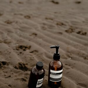 Two brown skincare bottles placed on a beach with wet sand and subtle footprints.