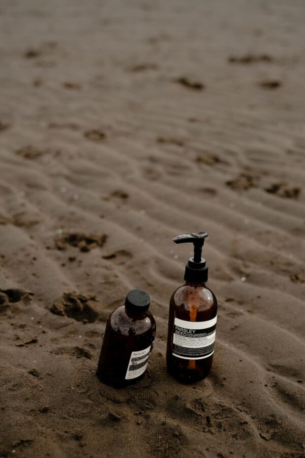 Two brown skincare bottles placed on a beach with wet sand and subtle footprints.