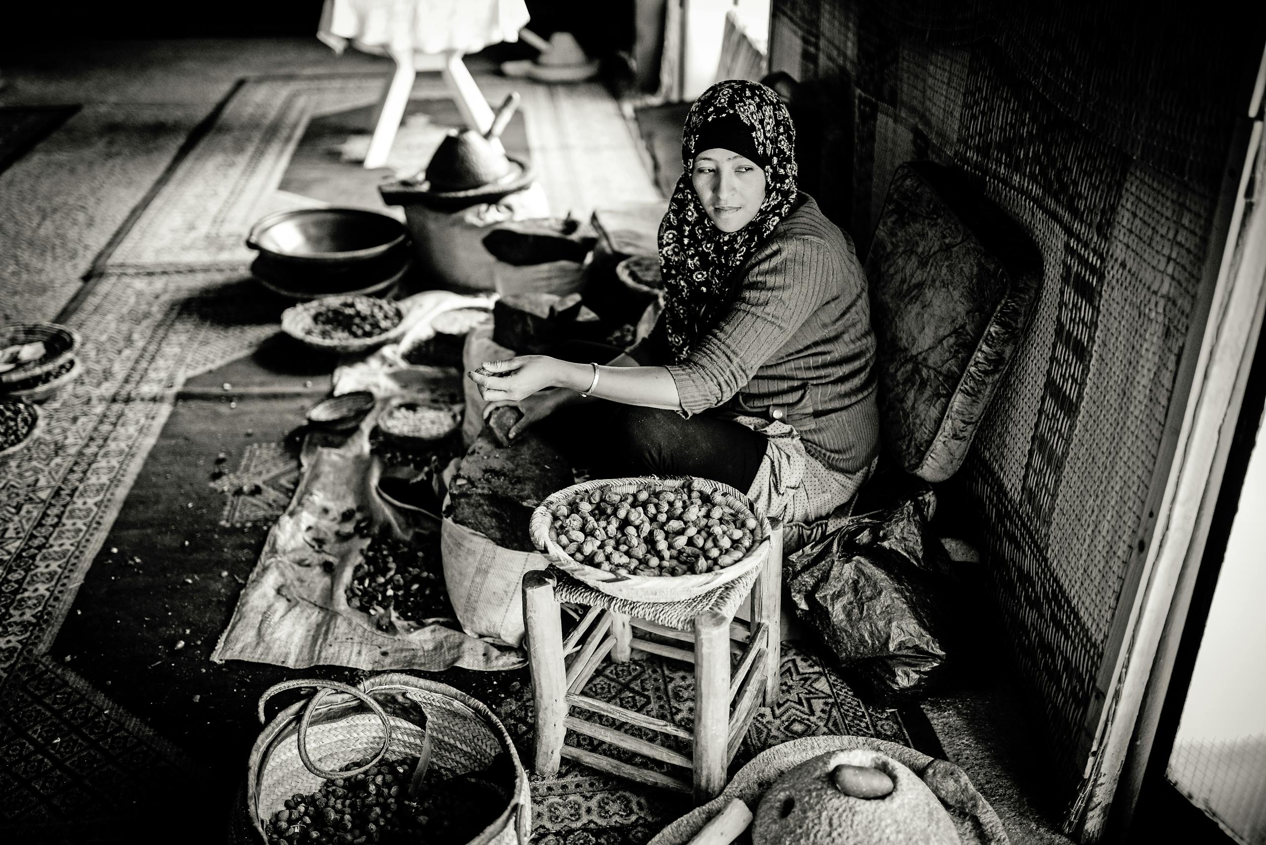 An Arab woman in a headscarf traditionally processes argan nuts. Black and white photography.